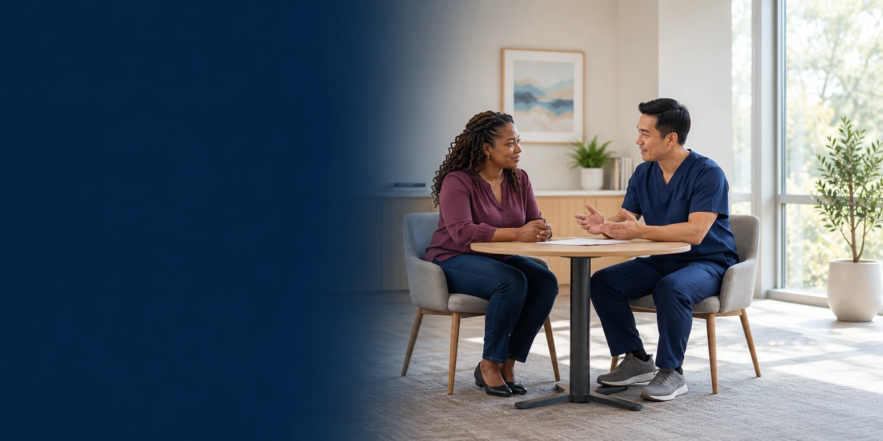 An adult patient and a clinician discuss care across a small table with a paper in front of them.