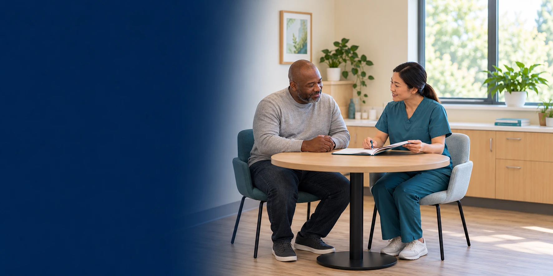 A patient and clinician sit together at a table reviewing an open notebook during a follow-up conversation.
